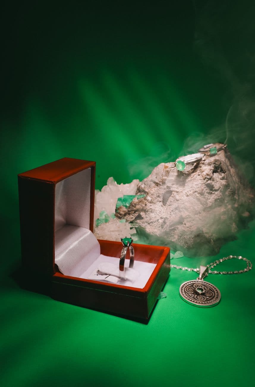 Elegant emerald jewelry set with a marble backdrop and silver pendant on green.