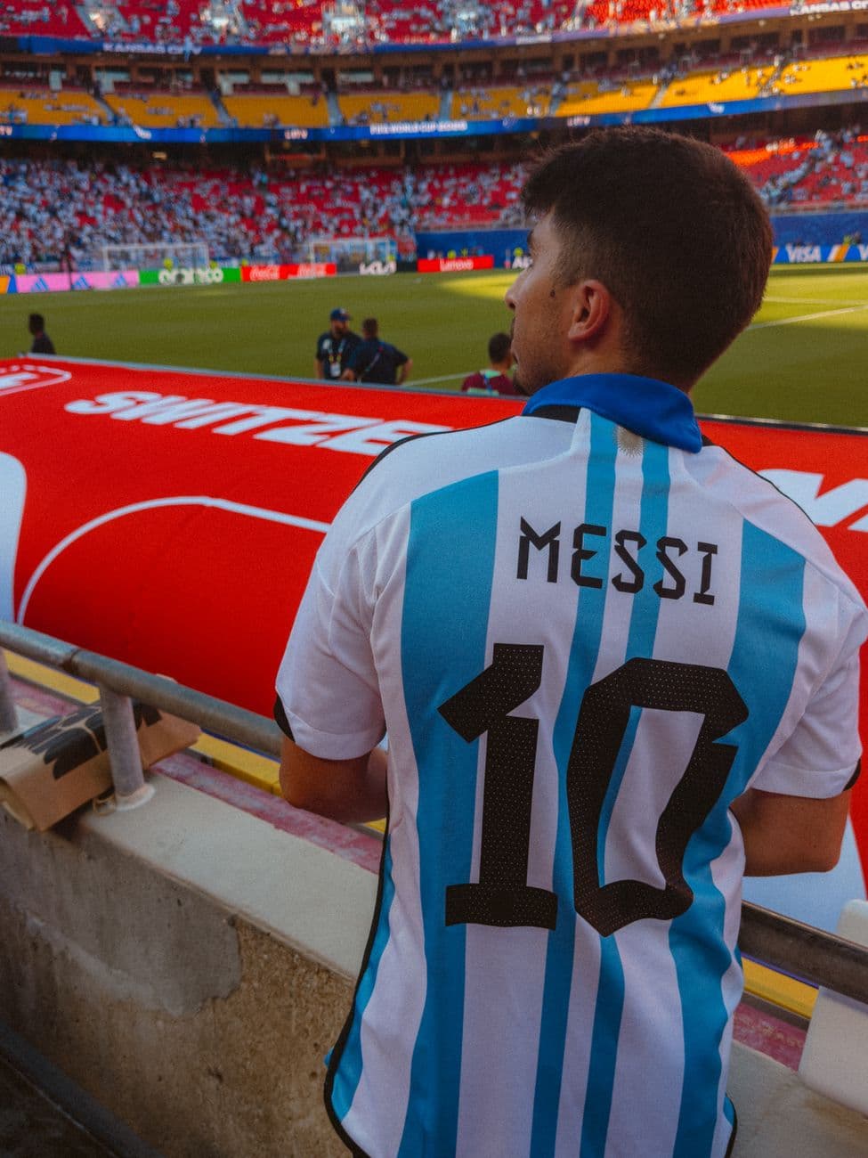 Fan in Argentina jersey with 'Messi 10' watching football match at crowded stadium.