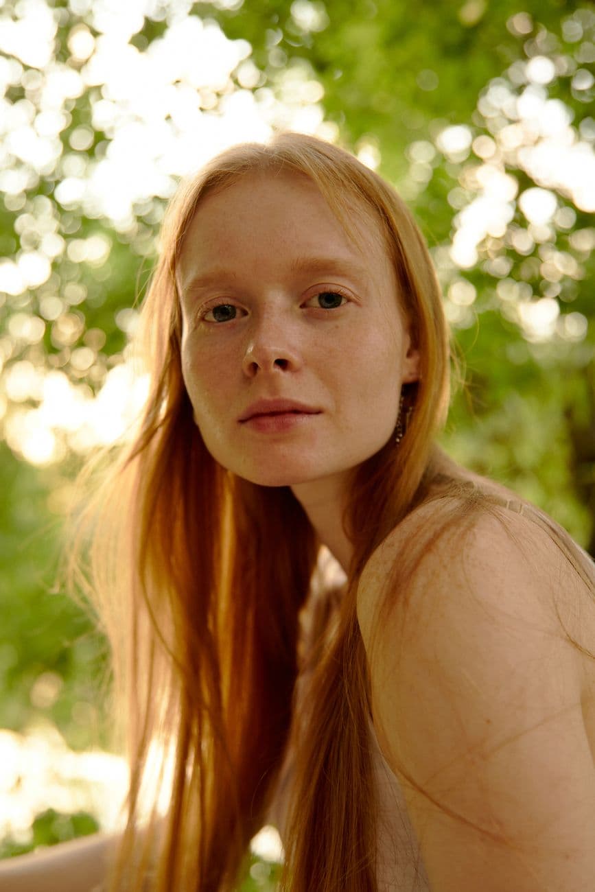 Gentle portrait of a woman with red hair in an outdoor setting, captured during daylight.
