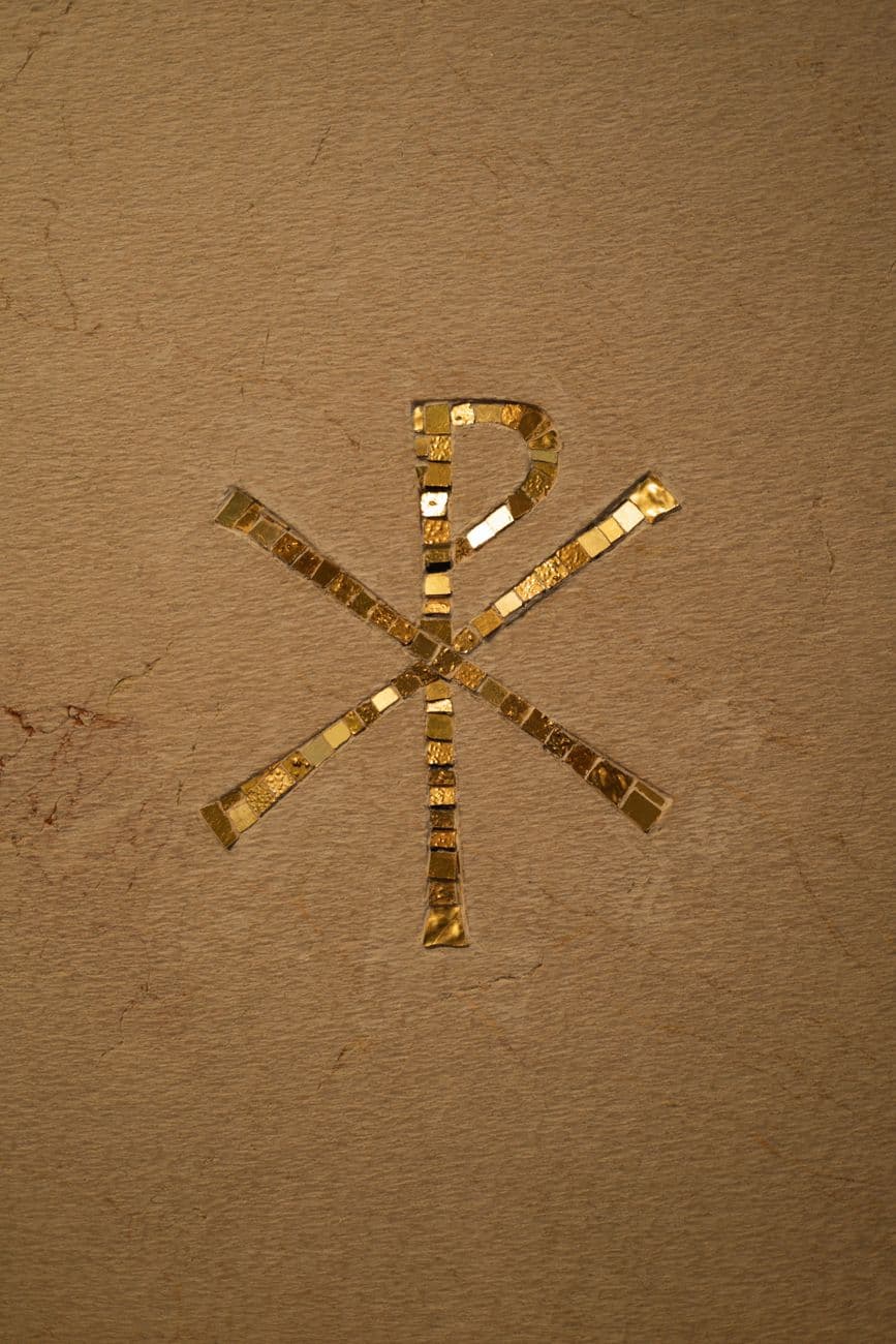 Golden Chi-Rho symbol intricately designed with mosaic tiles on a textured background, sym