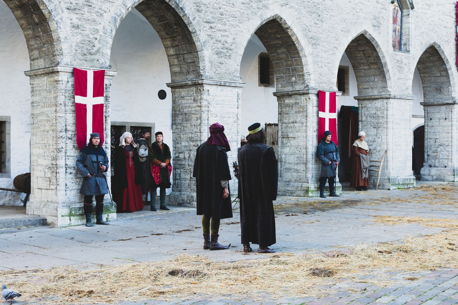Historic stone arches setting with people in medieval costumes during a reenactment.