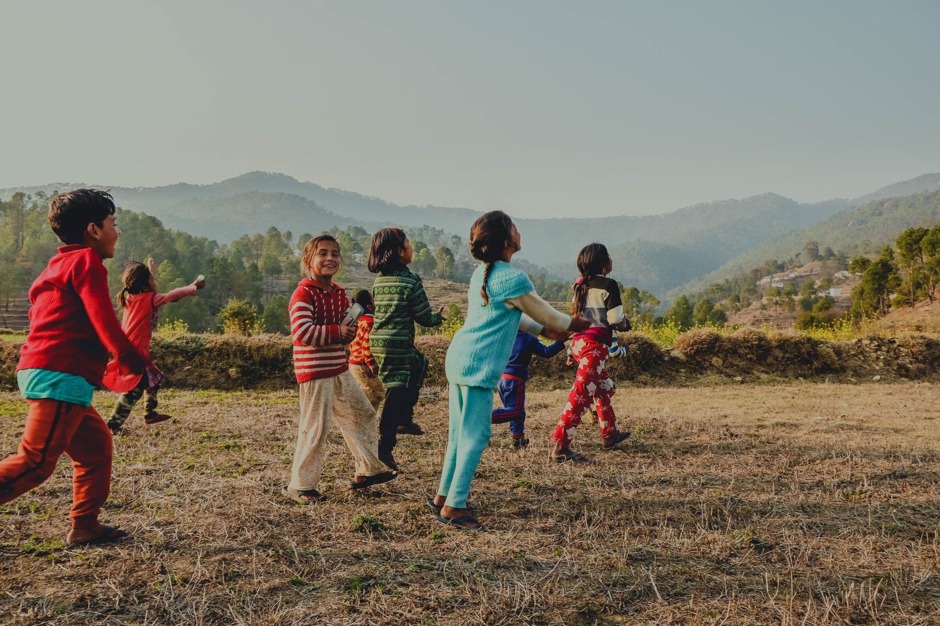 Joyful group of kids playing in a scenic mountain field in Uttarakhand, India at daytime.