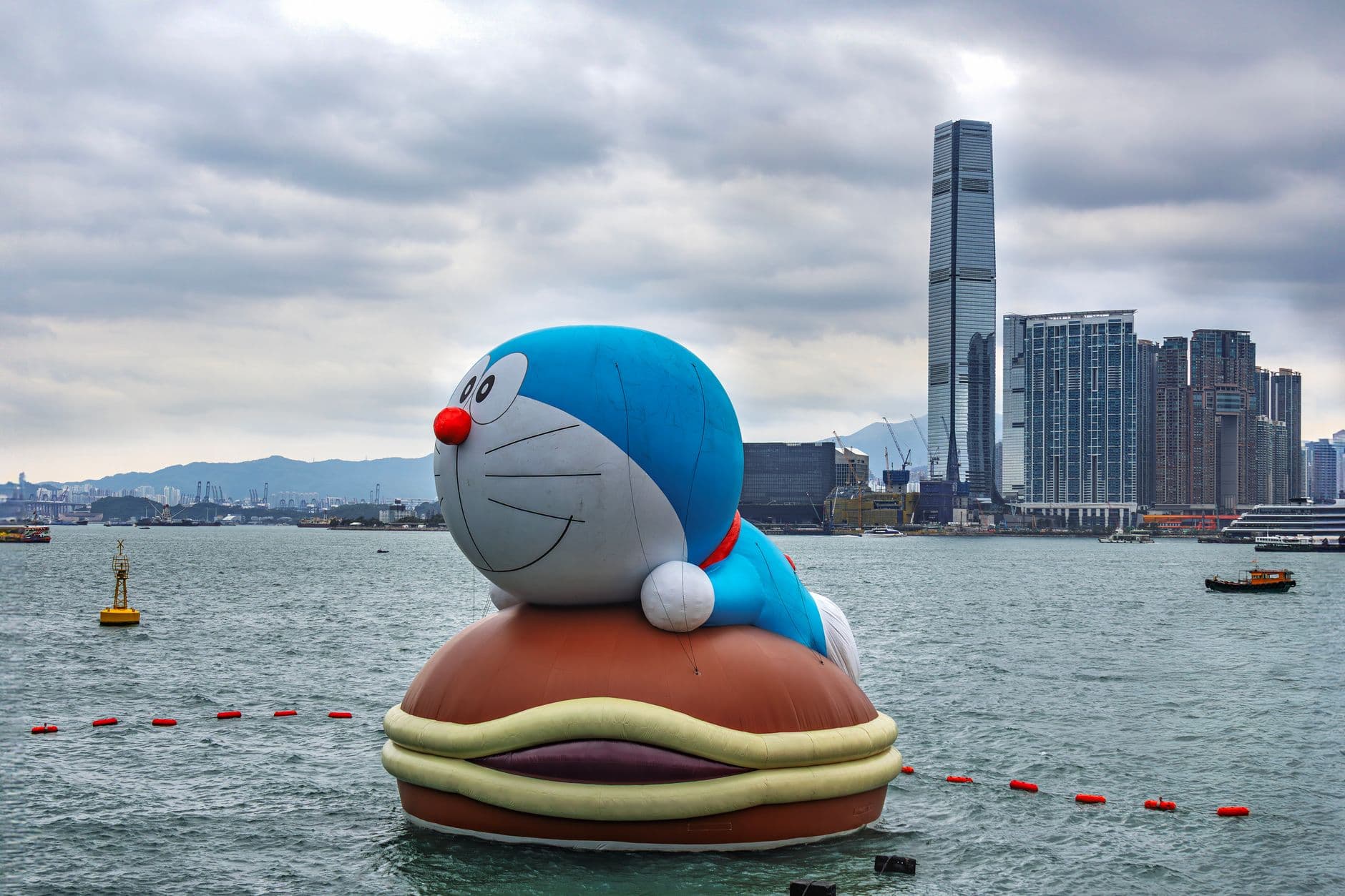 Large Doraemon float in Hong Kong Harbor with skyline and skyscrapers in the background.