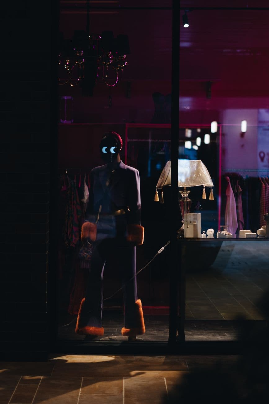 Mannequin with glowing eyes and fur trim inside a dimly lit boutique window display.