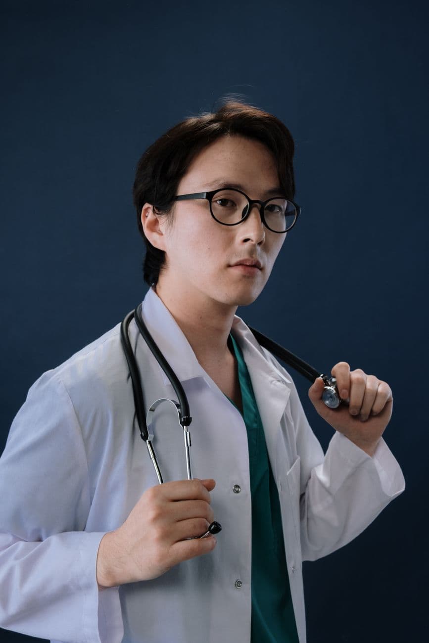 Portrait of a young male doctor in white coat with stethoscope in studio setting.