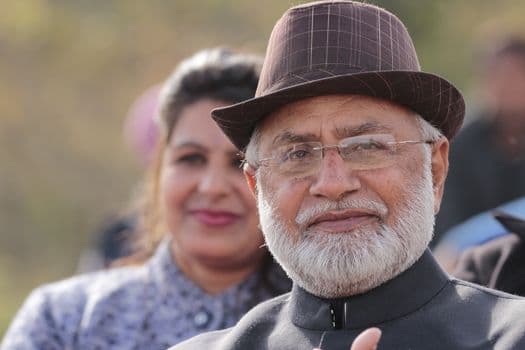 Portrait of an elderly man with a white beard wearing a hat outdoors with a woman in the b PNG