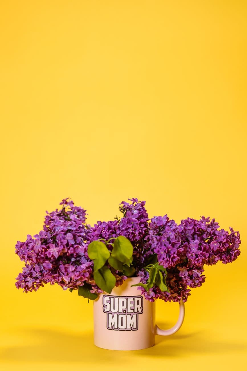 Purple flowers in a "Super Mom" mug on a yellow background, perfect for Mother's Day.