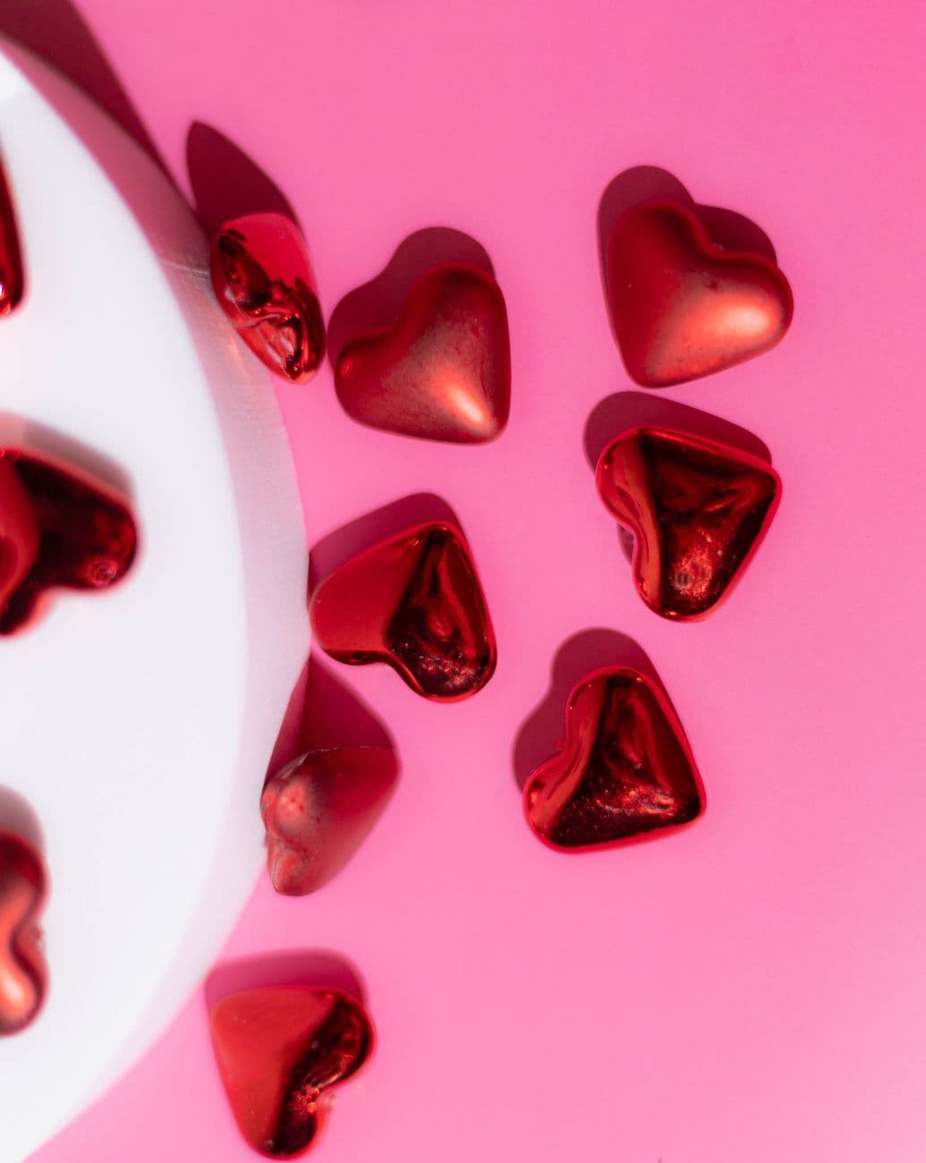 Romantic heart-shaped chocolates scattered on a vibrant pink surface, perfect for Valentin