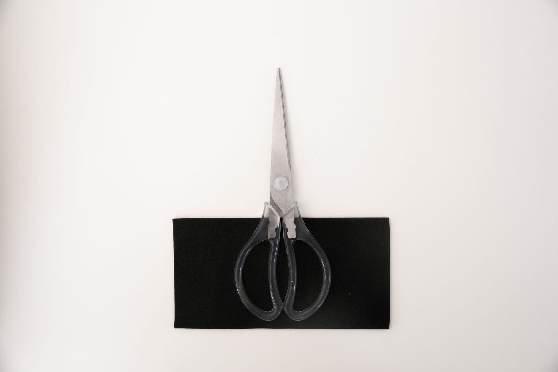 Sharp metal scissors placed on a black surface, captured from above on a white background.