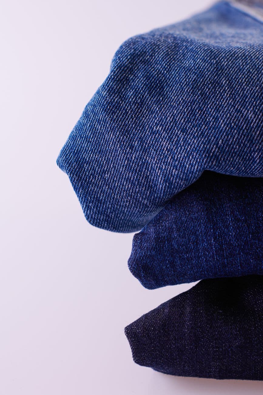 Stack of folded blue denim jeans on a white background showcasing texture and color variat