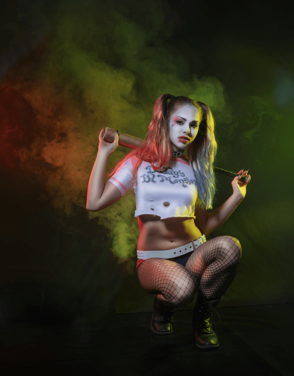 Stylized Harley Quinn cosplay photoshoot with colorful smoke effects in a dark studio sett