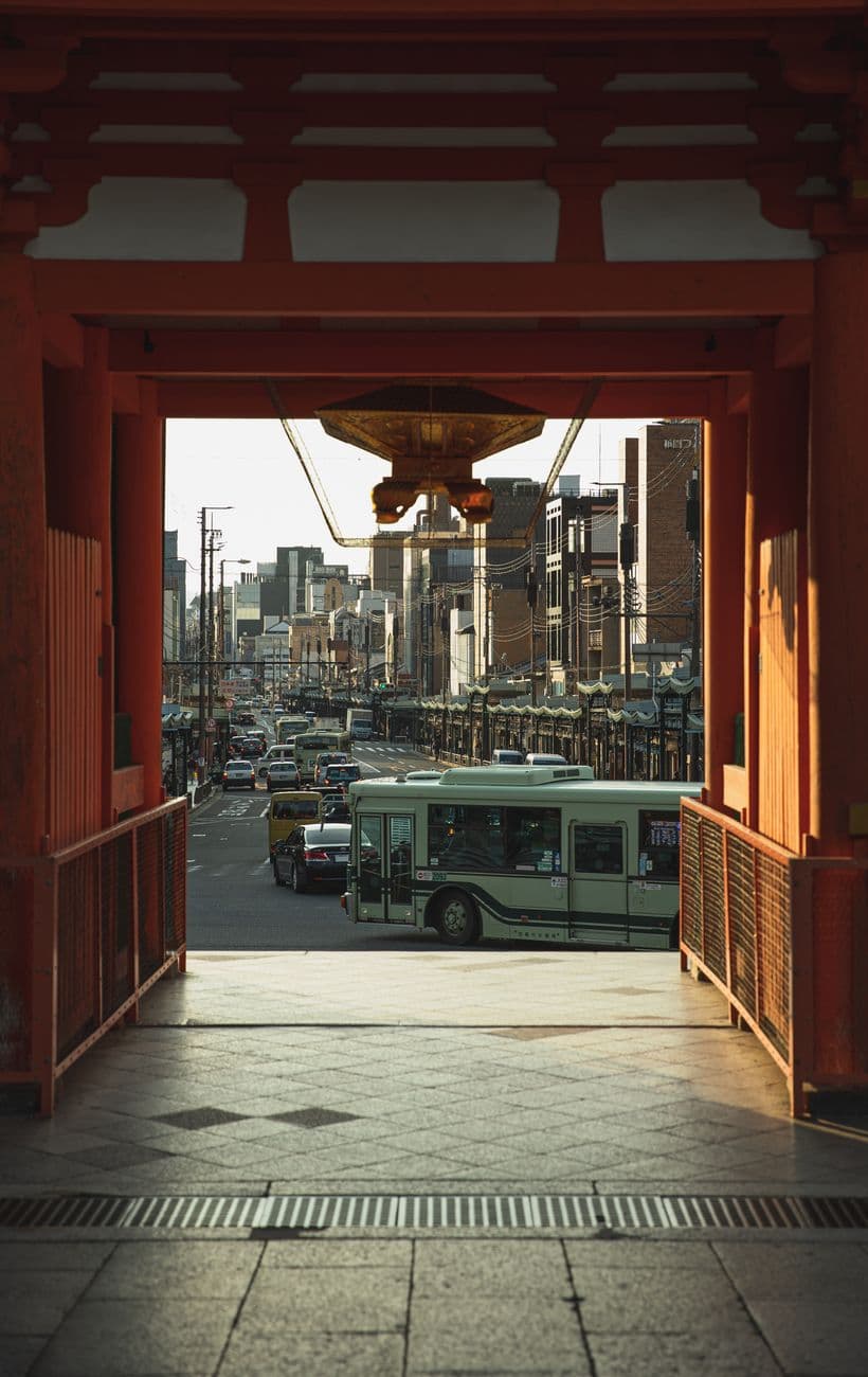 Through red gates of ancient Yasaka Shrine of various vehicles driving on road in Kyoto di