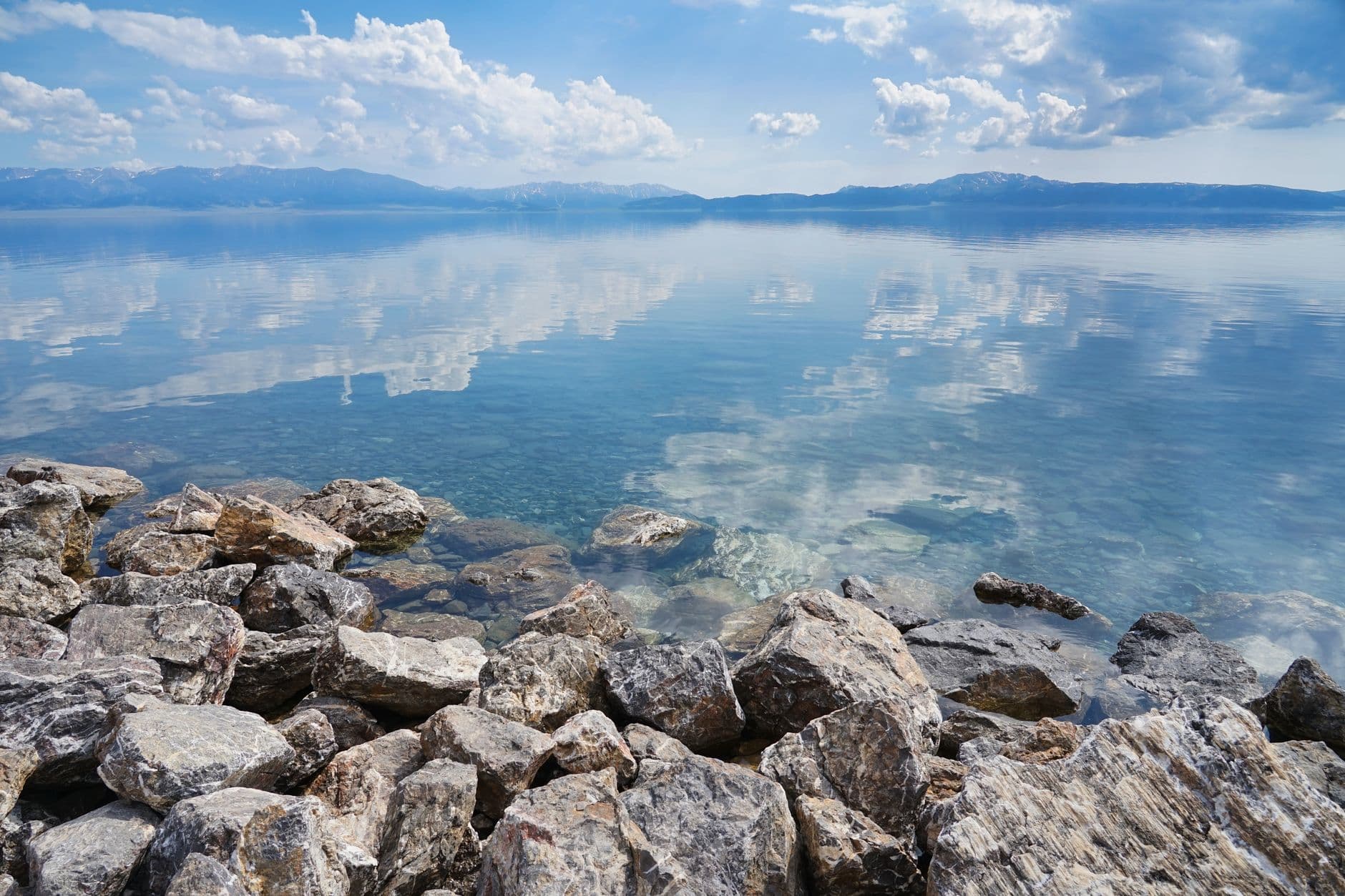Tranquil lake with clear reflections of mountains and clouds surrounded by rocky shore und