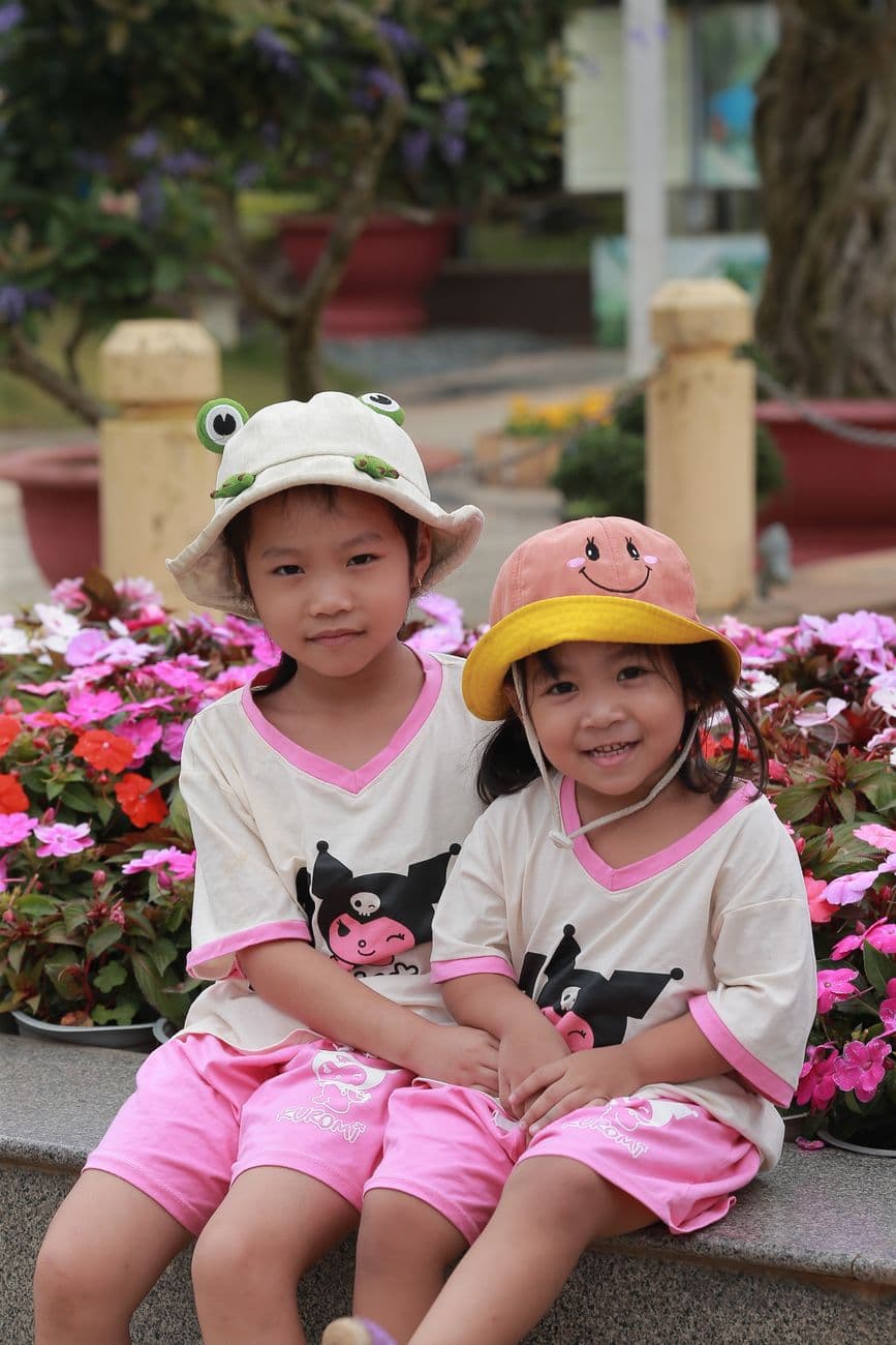 Two cheerful children in fun hats smiling among vibrant flowers, depicting pure innocence.