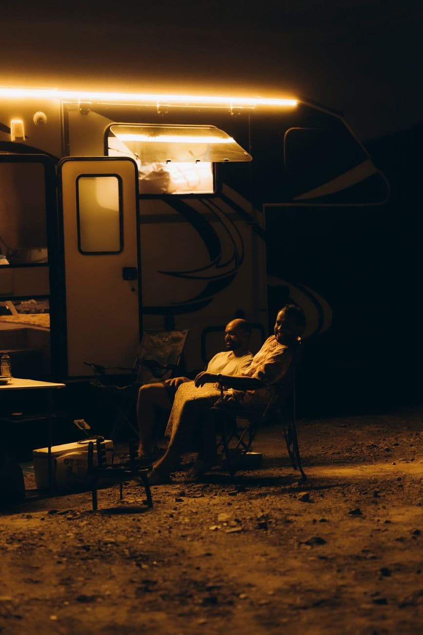 Two individuals enjoy a peaceful evening outside their RV, enveloped by warm light in Show