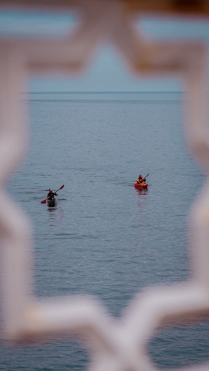 Two kayakers paddle across the serene waters of Llandudno, framed by an ornate structure.