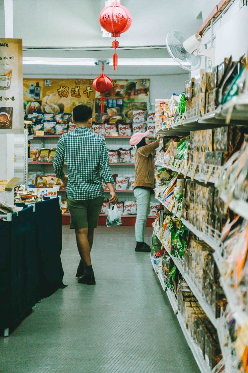 Two people shopping in an Asian grocery store in Kuala Lumpur, surrounded by shelves of pr