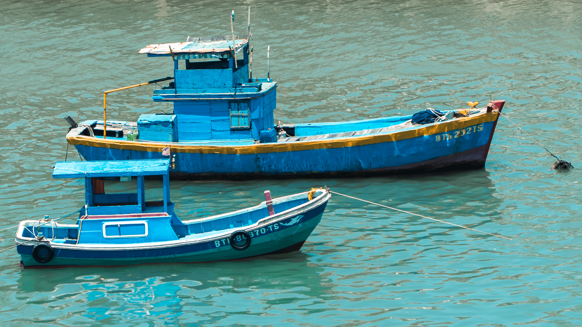 Two vibrant blue fishing boats anchored on serene turquoise waters, creating a tranquil sc