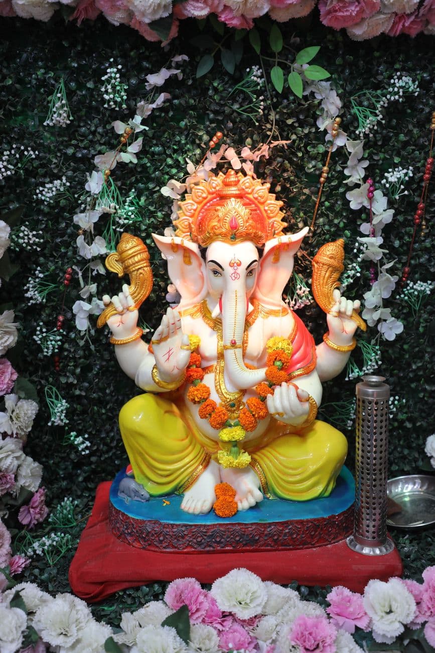 Vibrant Ganesh idol adorned with flowers and ornaments, set against a lush floral backdrop