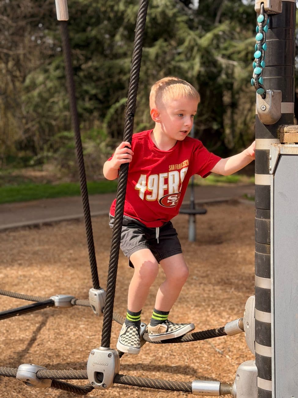 Young boy in red shirt climbs a rope structure at an outdoor playground. Daytime spring ac