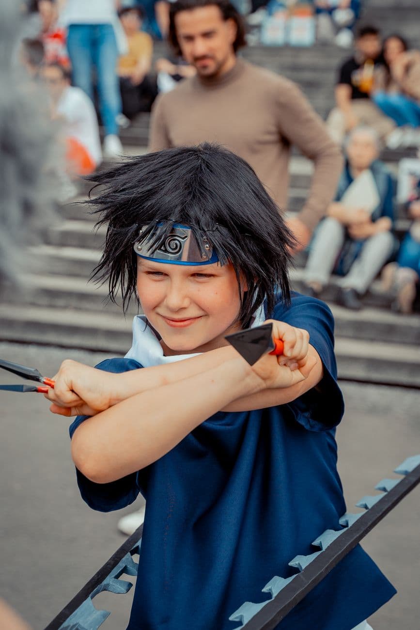 Young child in blue cosplay costume with knives, posing energetically outdoors in an urban