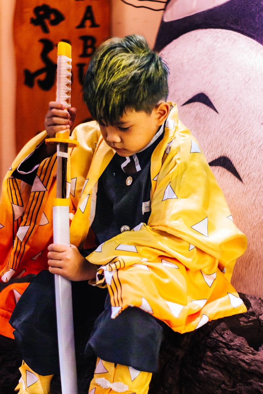 Young child in vibrant cosplay attire holding a sword, displaying a thoughtful expression.